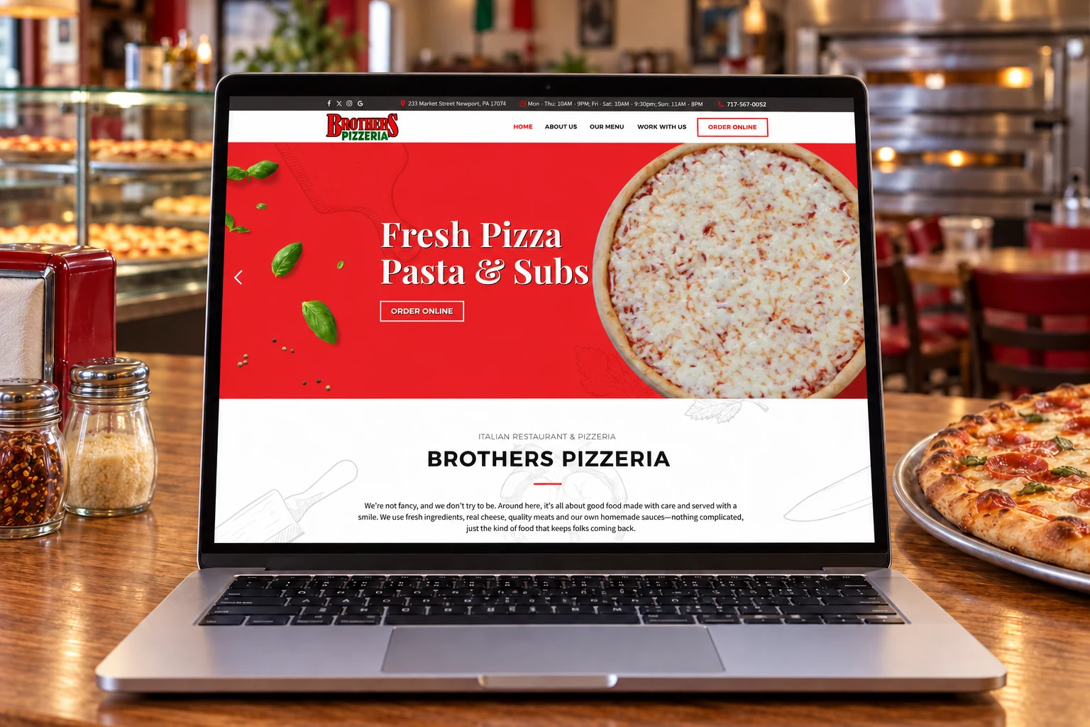 Open laptop showing a pizza restaurant website with a large pepperoni pizza on the screen in a pizzeria setting